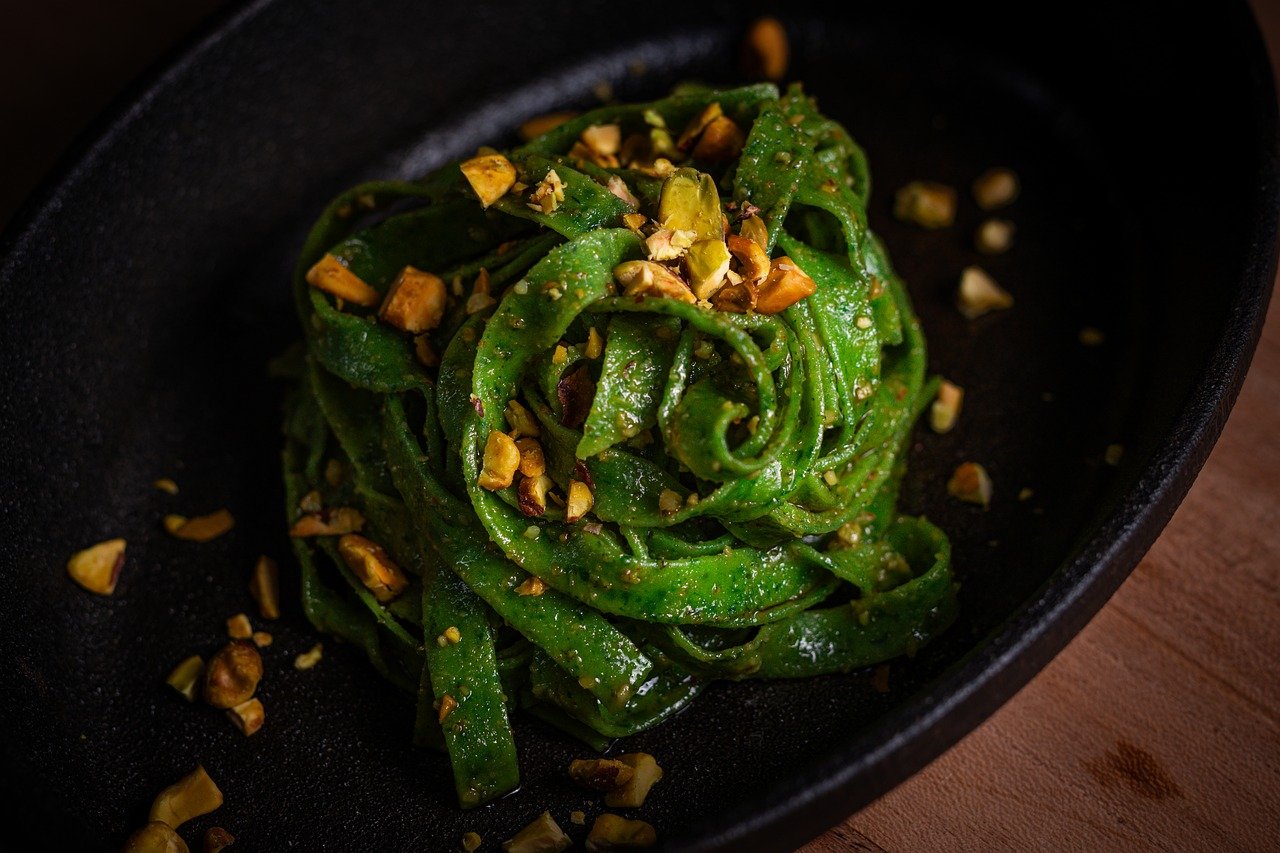 Pasta al pistacchio cremosa servita in un piatto, decorata con pistacchi tritati e una spruzzata di parmigiano.