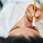 Truccatrice professionista mentre definisce le sopracciglia con matita e pennello.